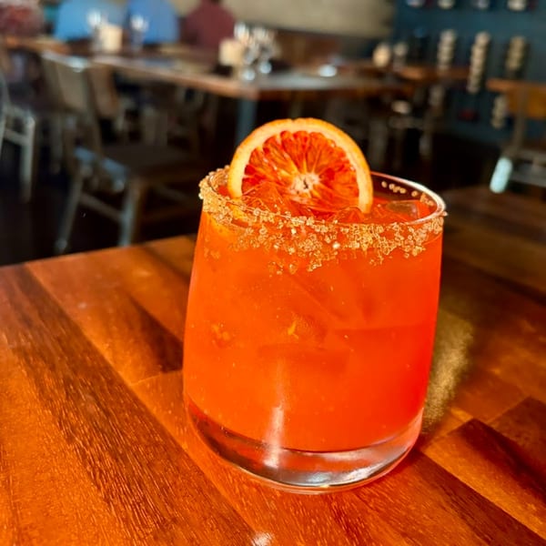 A vibrant orange cocktail with a sugared rim and a blood orange slice at Berkeley Cut Steakhouse.