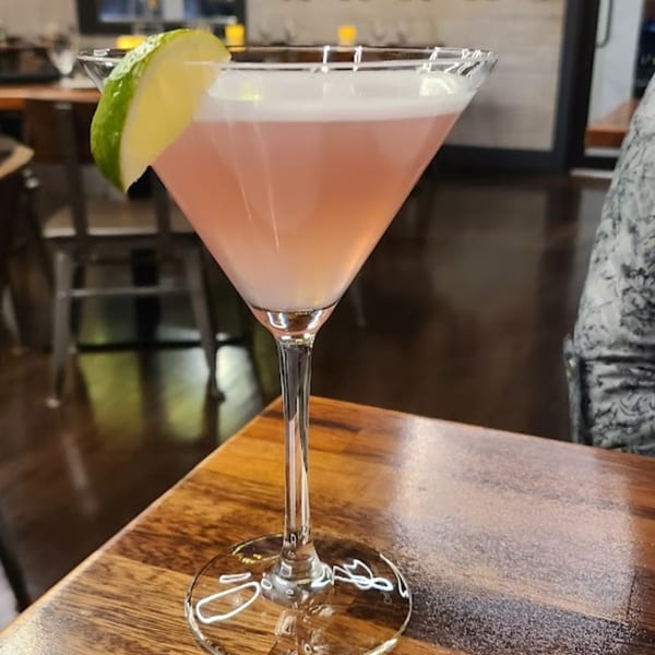 A pink martini with a lime wedge on a wooden table at Berkeley Cut Steakhouse.