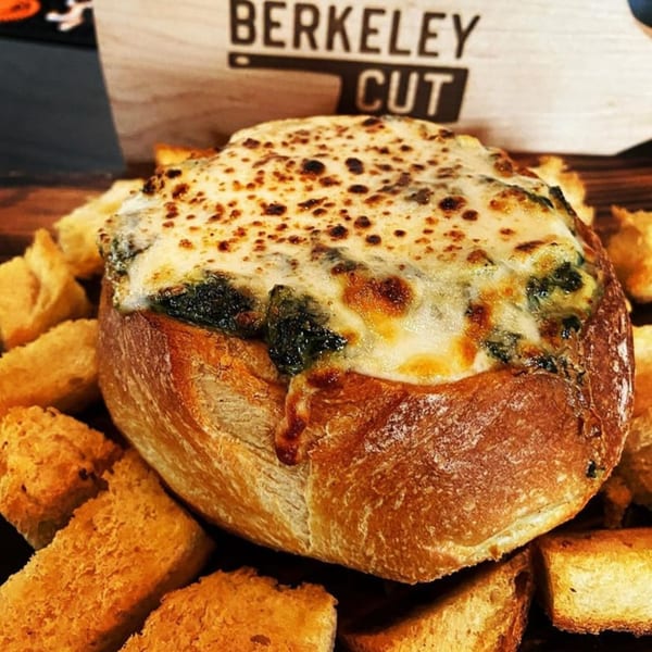 Spinach dip in a bread bowl with toasted bread pieces, Berkeley Cut logo in background.