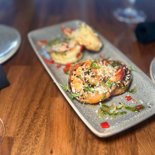 Grilled shrimp appetizer with sesame seeds, herbs, and red peppers on a gray plate at Berkeley Cut Steakhouse.