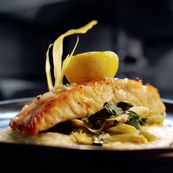 Pan-seared salmon with lemon, creamy sauce, and sauteed greens on a dark plate.