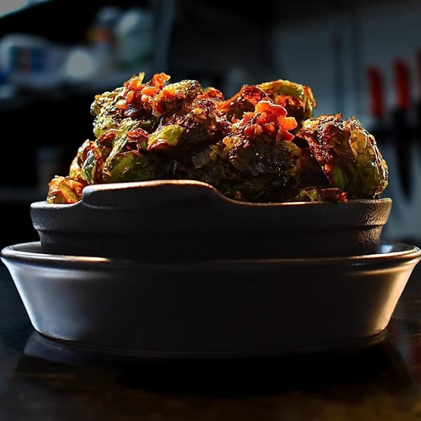 A dark bowl filled with crispy Brussels sprouts topped with red chili flakes at Berkeley Cut Steakhouse.