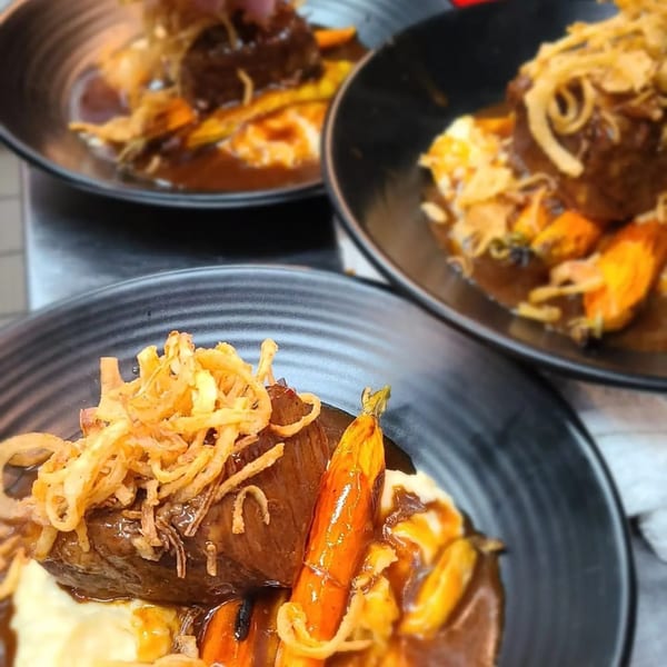 Three plates of Berkeley Cut Steakhouse short ribs with mashed potatoes, carrots, and crispy onions.