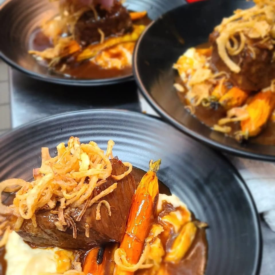 Three plates of Berkeley Cut Steakhouse short ribs with mashed potatoes, carrots, and crispy onions.