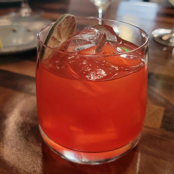 A vibrant red cocktail with ice and a dried lime slice, on a wooden table at Berkeley Cut Steakhouse.