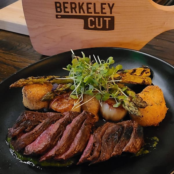 Sliced steak with grilled asparagus, roasted potatoes, and microgreens on a black plate.